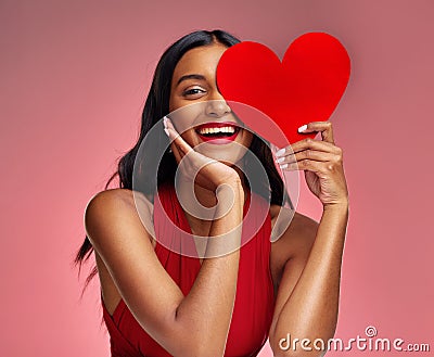 Woman, paper heart and smile in studio portrait for makeup, beauty or romantic sign by red background. Happy girl Stock Photo