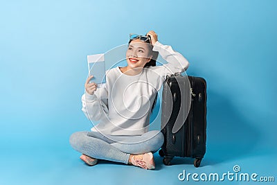 A woman with a passport and a ticket sits on the floor near a black suitcase in sunglasses Stock Photo