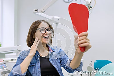 Woman patient looking in the mirror at the teeth, sitting in the dental chair. Healthcare, medical and dentistry concept Stock Photo