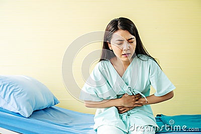 Woman patient suffering from stomach ache while sitting on bed at hospital, abdominal pain, food poisoning Stock Photo