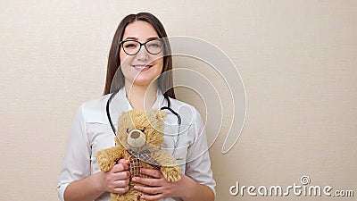 Woman pediatrician with glasses holds teddy bear on beige Stock Photo