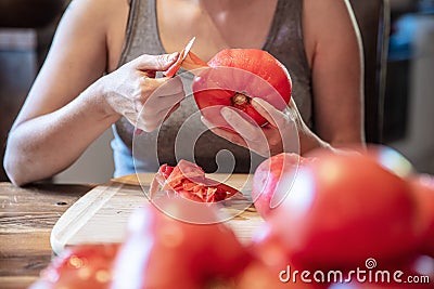 Woman is peeling a lot of red fresh and boiled tomatos with a knife, preparing for cooking a sauce Stock Photo