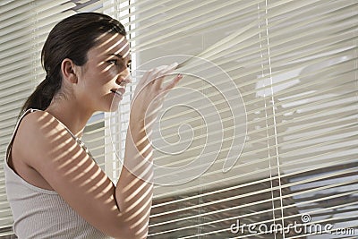 Woman Peering Through Blinds At Home Stock Photo