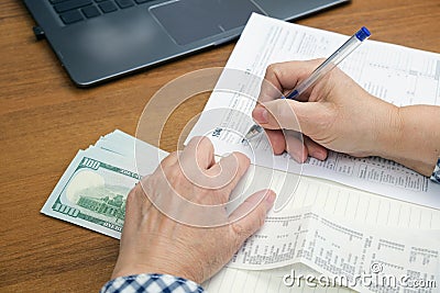 woman with a pen in her hands at a table with a wad of cash dollars calculates income for taxes Stock Photo