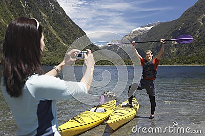 Woman Photographing Man Raise Oar At Mountain Lake Stock Photo