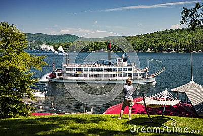 WOMAN PHOTOGRAPHING PADDLE STEAM BOAT ON LAKE FROM SHORE Editorial Stock Photo