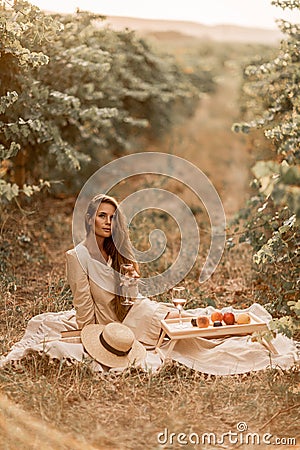 Woman picnic vineyard. Romantic dinner, fruit and wine. Happy woman with a glass of wine at a picnic in the vineyard on Stock Photo