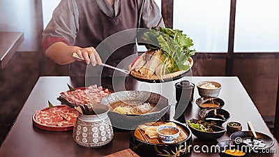 A woman pinching vegetables into hot pot by tongs with Wagyu A5 beef and sliced Kurobuta in Shabu clear soup with stream Stock Photo