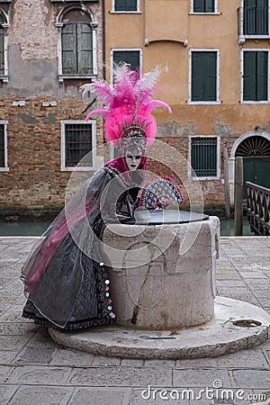 Masked woman in pink and black hand made costume with fan and ornate painted feathered mask at Venice Carnival Editorial Stock Photo