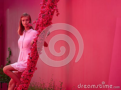 Woman in a pink dress on a bright pink street sits on a staircase decorated with flowers Stock Photo