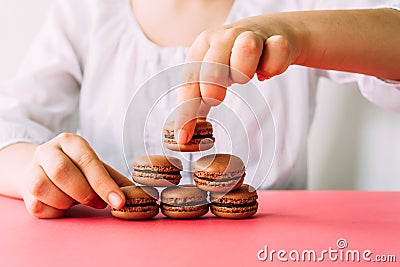 Woman placing macaroons on heap on pink table Stock Photo