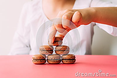 Woman placing macaroons on heap on pink table Stock Photo