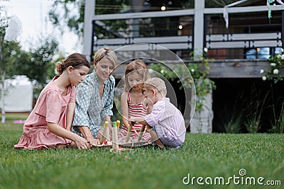 Woman playing with kids in the garden, outdoor garden games, sitting on grass. Stock Photo