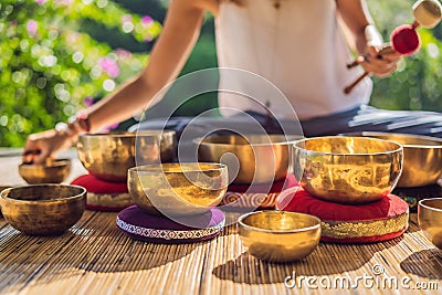 Woman playing on Tibetan singing bowl while sitting on yoga mat against a waterfall. Vintage tonned. Beautiful girl with Stock Photo