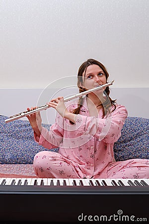 A woman plays a flute sitting on a home bed at an electric piano Stock Photo
