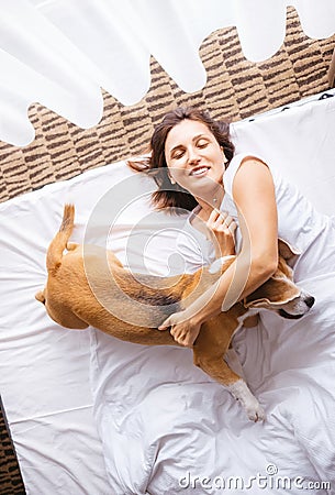 Woman plays with her beagle dog in bed in morning time Stock Photo