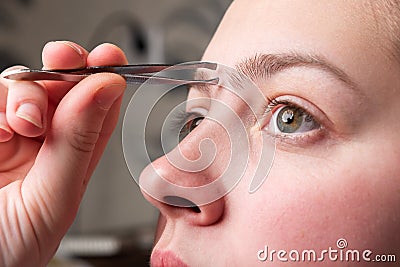 Woman plucking eyebrows with tweezers. Stock Photo