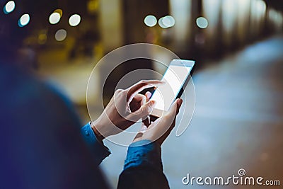 Woman pointing finger on blank screen smartphone on background bokeh light in night atmospheric city, hipster blogger using in han Stock Photo