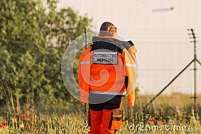 Woman a polish ambulance worker standing back in medical orange uniform with inscription Emergency medical Services. Editorial Stock Photo