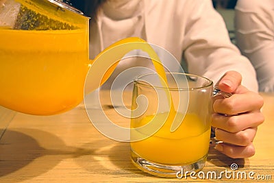 Woman is pouring buckthorn herbal tea to cup from teapot, hands closeup. Stock Photo