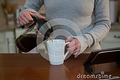 Woman pouring coffee into mug in kitchen Stock Photo