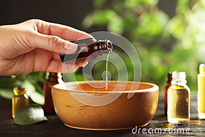 Woman pouring essential oil from glass bottle into bowl on table Stock Photo