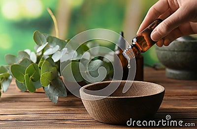 Woman pouring eucalyptus essential oil into bowl on wooden table Stock Photo