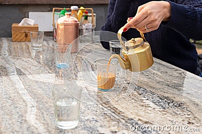 Woman pouring masala tea from teapot into cupglass on table in cafe. Stock Photo