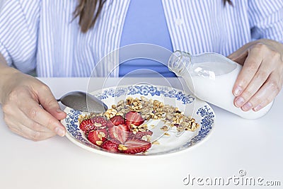 Woman pouring plant based milk into homemade granola with fresh organic strawberries and yogurt in the vintage plate. Stock Photo