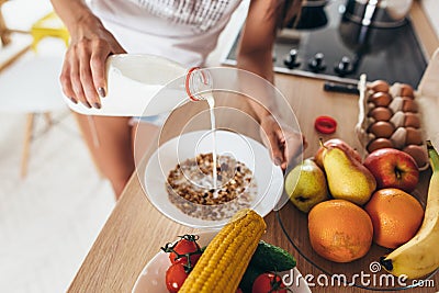 Woman pours milk into a bowl. Muesli fruits vegetables. Stock Photo