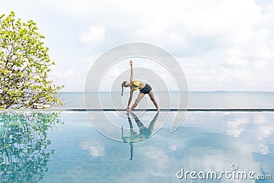 Woman practice yoga Triangle pose to meditation summer vacation on the pool above the beach,Travel in tropical beach Stock Photo