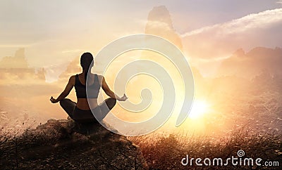 Woman practices meditating yoga at is an asana on a stone, sunset mountains background Stock Photo