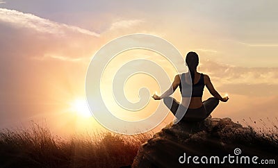 Woman practices meditating yoga at is an asana on a stone, sunset mountains background Stock Photo