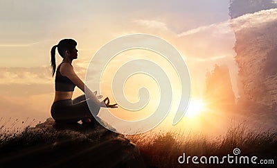 Woman practices meditating yoga at is an asana on a stone, sunset Stock Photo