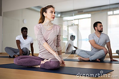 Woman practicing Parivritta Ardha Padmasana during group yoga training Stock Photo