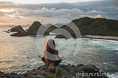 Woman practicing yoga in lotus pose at sunset with beautiful ocean view Stock Photo