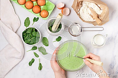 Woman prepares dough for homemade green pancakes for Breakfast. Whisk for whipping in hands Stock Photo