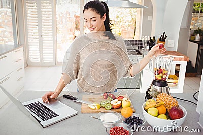 Woman preparing fruit juice while working on laptop Stock Photo