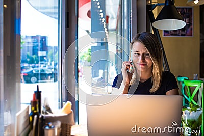 Woman professional advertiser talking on mobile phone with client and reading information on laptop computer Stock Photo