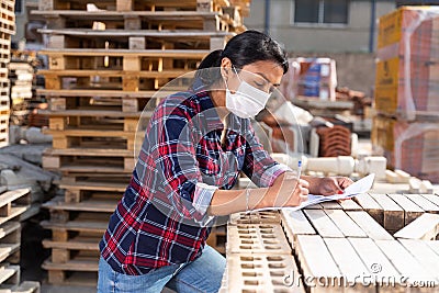 Woman in protective face mask controlling quantity of redbricks Stock Photo