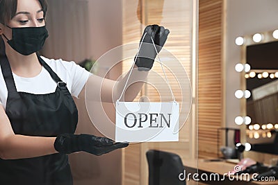 Woman with protective mask hanging Open sign onto door in salon. Beauty services during Coronavirus quarantine Stock Photo