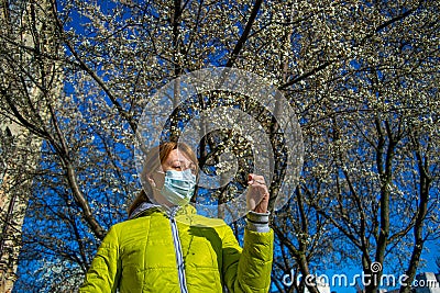 The woman in the protective mask in a park near the blossoming, magnolia tree wants to smell flowers on a sunny spring day Stock Photo