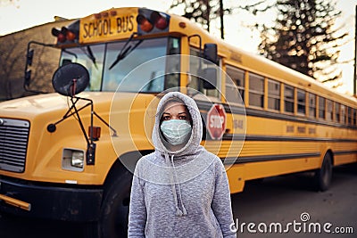 A woman in a protective mask stands on the background of a school bus. A large stop sign is visible on the background Stock Photo