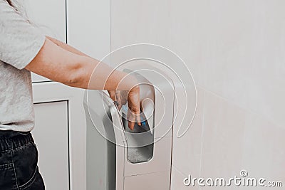 A woman in a public place dries her hands in an electric dryer. Precautions and protection for coronavirus Stock Photo