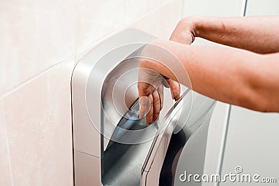 A woman in a public place dries his hands in an electric dryer Stock Photo