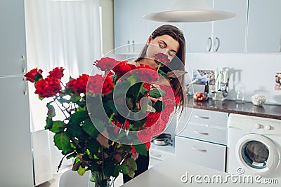 Woman puts roses in vase smelling flower. Housewife taking care of coziness on kitchen. Modern kitchen design Stock Photo
