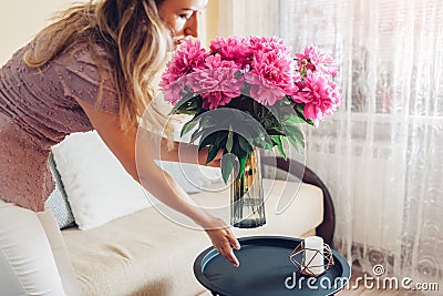 Woman puts vase with peonies flowers on table. Housewife taking care of coziness at home. Interior and spring decor Stock Photo