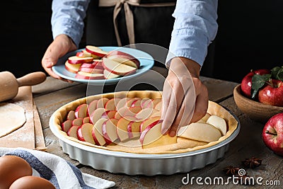 Woman putting apple slices into dish with raw dough at wooden table, closeup. Baking pie Stock Photo