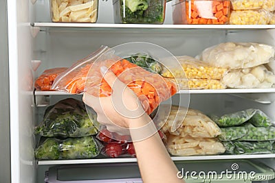 Woman putting bag with carrot in refrigerator with frozen vegetables, closeup Stock Photo