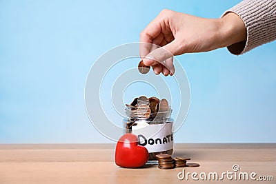 Woman putting coin into jar with label DONATE on table against color background, closeup. Stock Photo